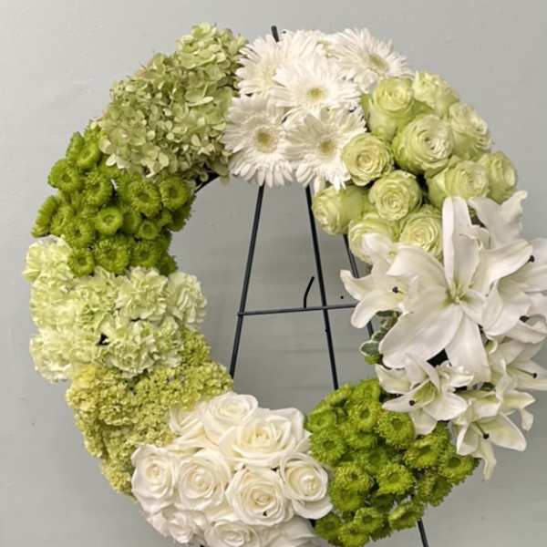 Circular floral wreath with white and green flowers on a black stand