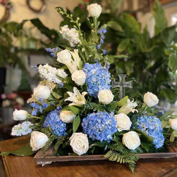Blue hydrangeas and white roses arranged with a clear cross centerpiece