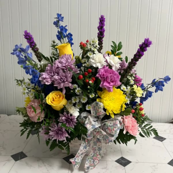 Colorful mixed flower arrangement in a white basket with a floral ribbon