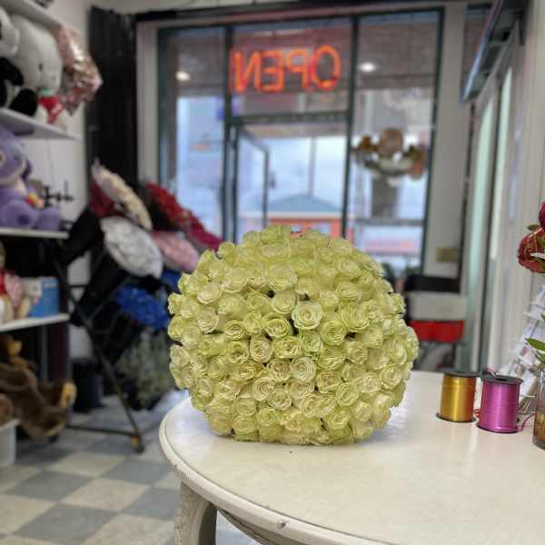 Round ball arrangement of pale yellow roses displayed on a white table in a flower shop