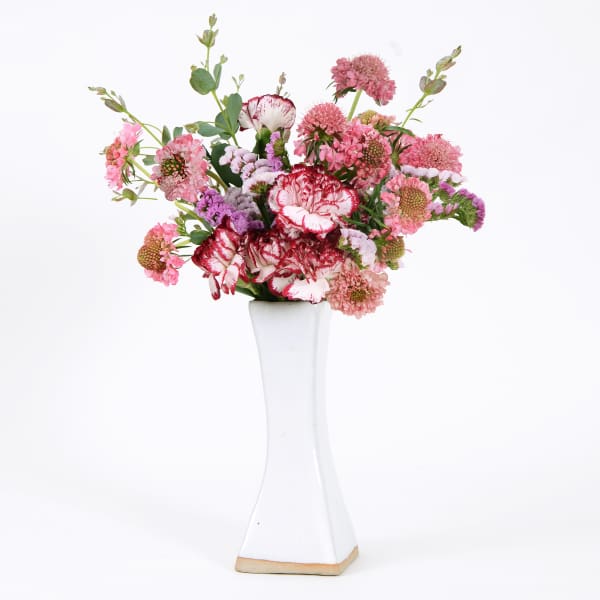 Pink and red mixed flowers arranged in a tall white vase