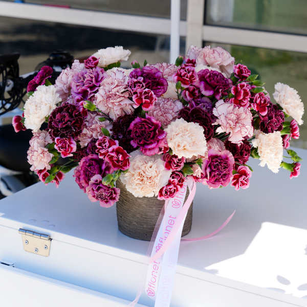 Bouquet of pink and white carnations in a round container with a ribbon