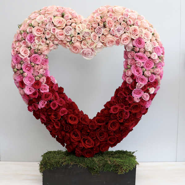 Large open heart of pink and red roses on a moss-covered base in a rectangular black container