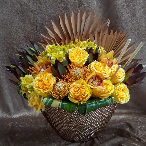Yellow roses and orchids arranged in a textured basket with decorative leaves