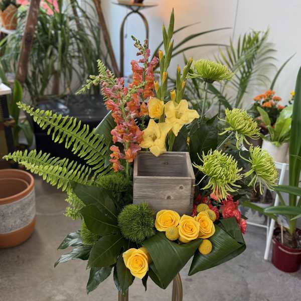 Tropical floral arrangement with yellow roses and green blooms in a wooden box