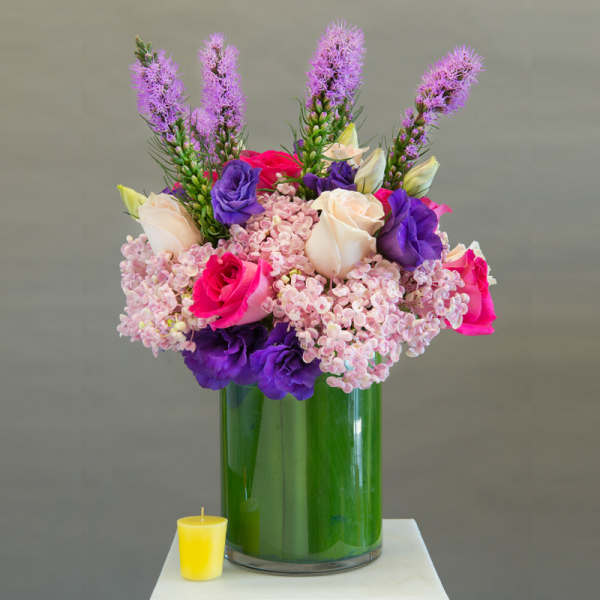 Pink, purple, and cream roses in a tall glass vase with a small yellow candle nearby