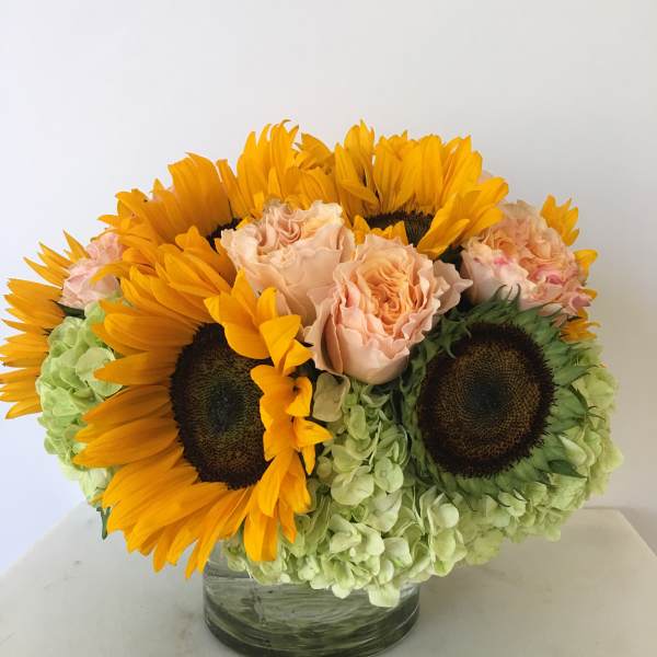 Sunflowers, pale roses, and green hydrangeas in a glass vase