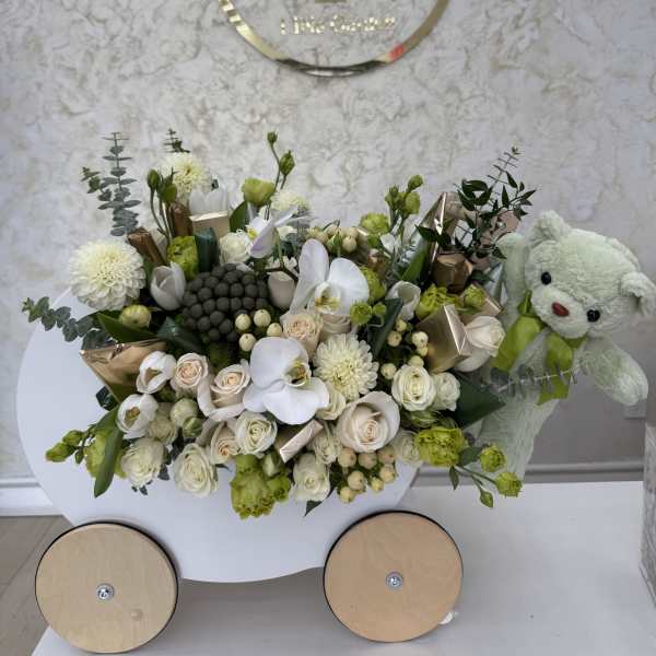 White and green floral arrangement with a teddy bear in a cart