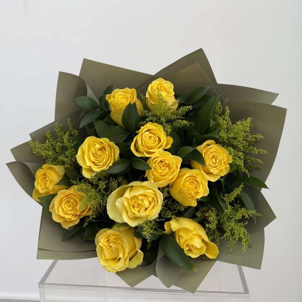 Bouquet of yellow roses with dark green foliage and olive wrapping