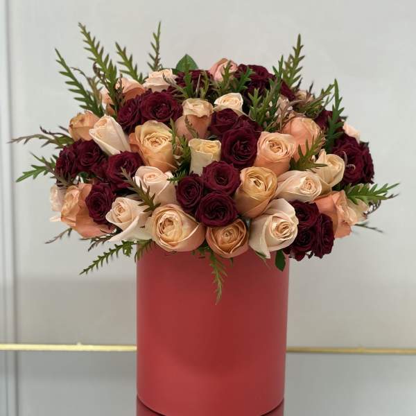 Bouquet of peach and burgundy roses in a red cylindrical vase