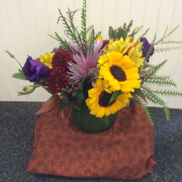 Mixed bouquet with sunflowers, purple blooms, and red flowers in a green vase