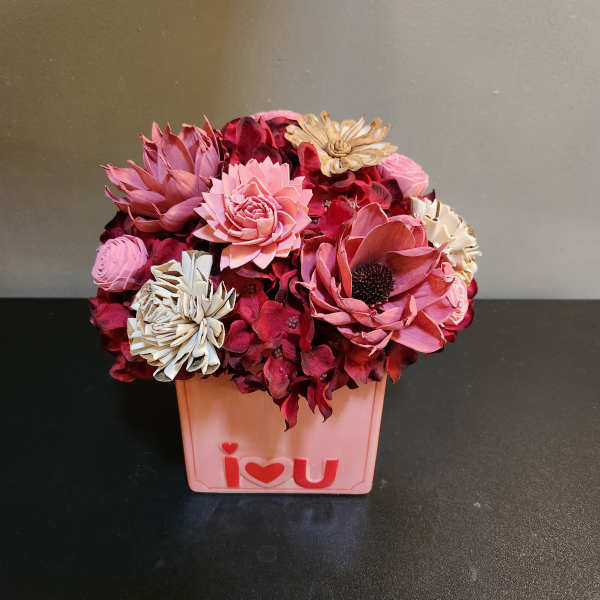 Pink and burgundy flowers arranged in a small box with an "I love you" front