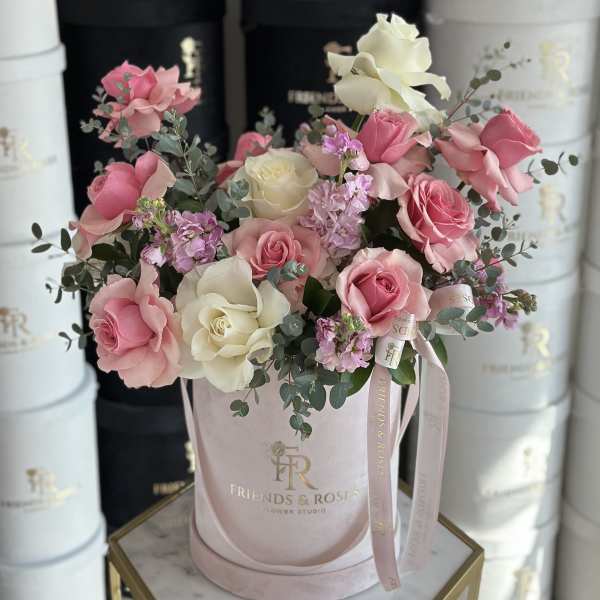 Pink and white roses arranged in a pale pink hatbox with ribbon.