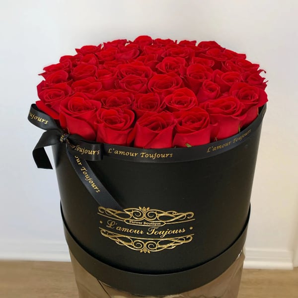 Round box filled with red roses and tied with a black ribbon