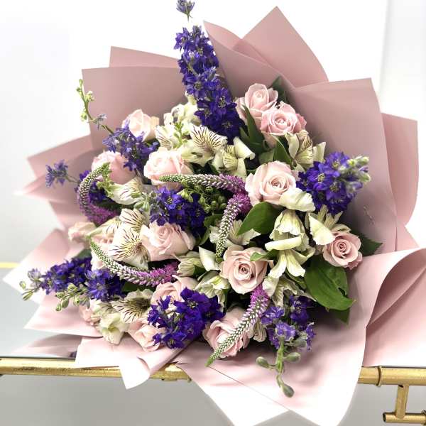 Bouquet of pink roses, purple flowers, and white blooms wrapped in blush paper