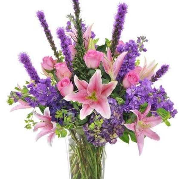 Pink lilies and roses in a clear glass vase with purple flowers