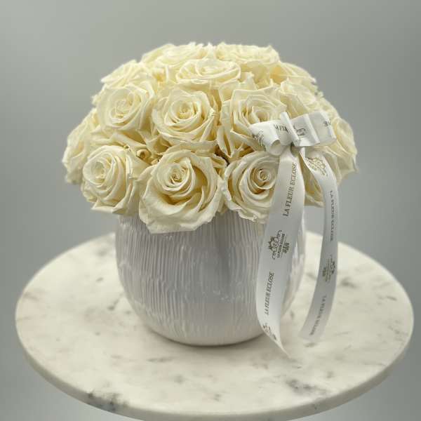 Cream rose bouquet in a white textured vase with a ribbon bow