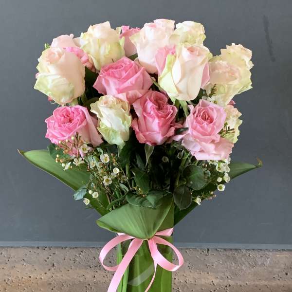 Bouquet of pink and white roses in a tall glass vase with a pink ribbon