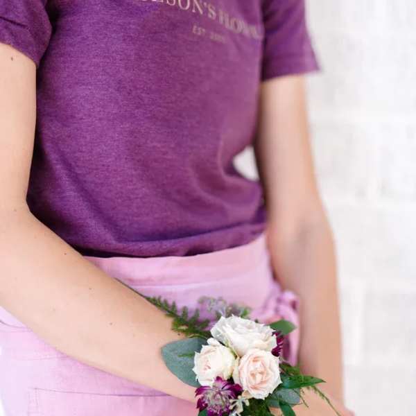 Person wearing a small wrist corsage with pale roses and purple flowers