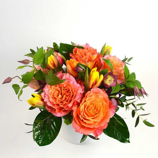 Orange and pink roses with yellow tulips in a white vase