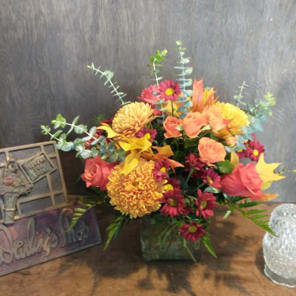 Mixed bouquet in a square glass vase with pink, orange, and yellow flowers