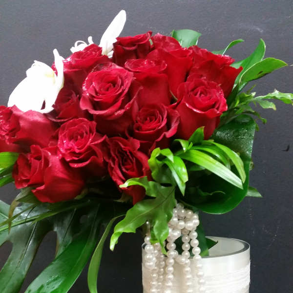 Red roses in a tall glass vase with white bead strands