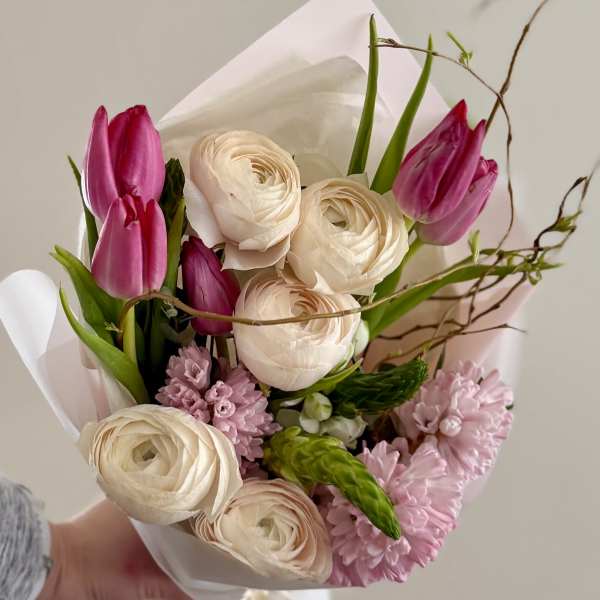 Hand-tied bouquet of pink tulips and cream ranunculus wrapped in white paper