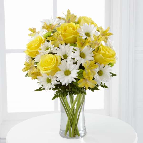 Yellow roses and white daisies in a clear glass vase
