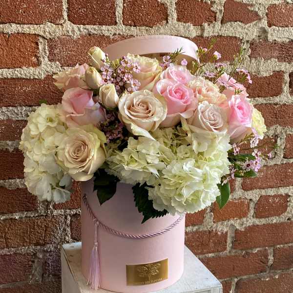 Pink and cream roses with white hydrangeas in a pink hatbox