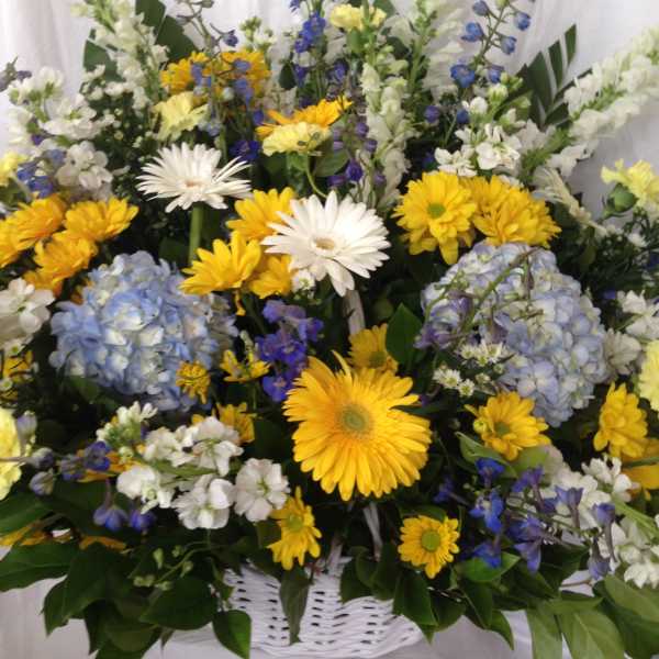 Mixed yellow, white, blue, and lavender flowers in a white basket