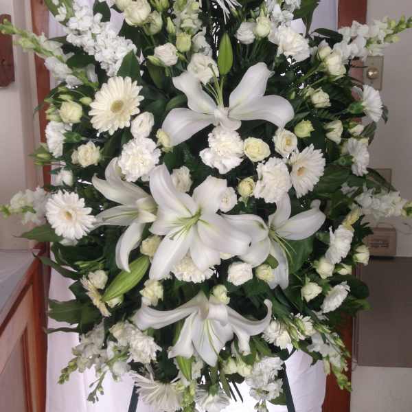 Large white funeral spray with lilies, daisies, and roses on an easel