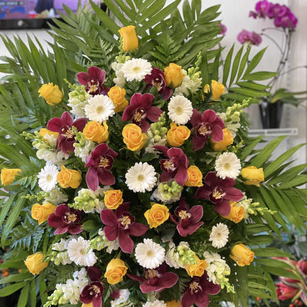 Large standing spray with yellow roses, burgundy orchids, and white daisies