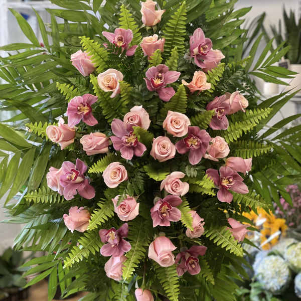 Pink roses and orchids arranged in a tall standing display with fern foliage.