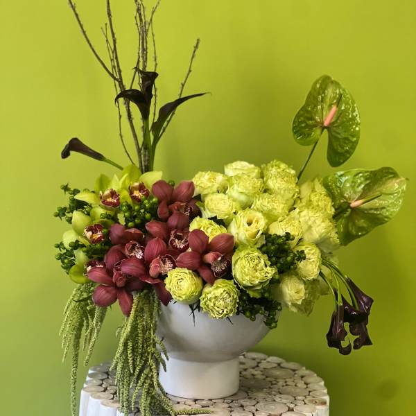 Floral arrangement with green and burgundy orchids in a white vase