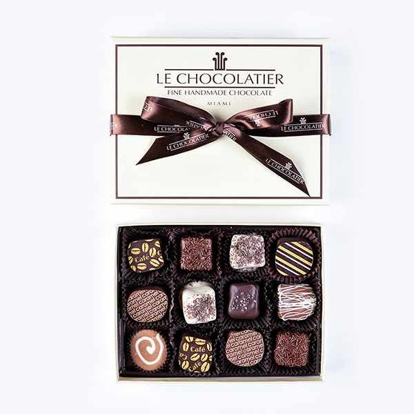 Box of assorted gourmet chocolates with lid and ribbon beside it