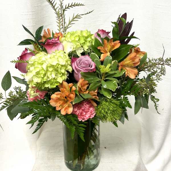 Mixed bouquet of green hydrangeas, pink roses and carnations, and orange alstroemeria in a glass vase