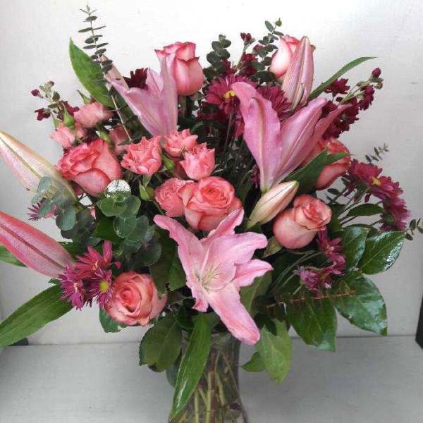 Pink roses and lilies arranged in a clear glass vase