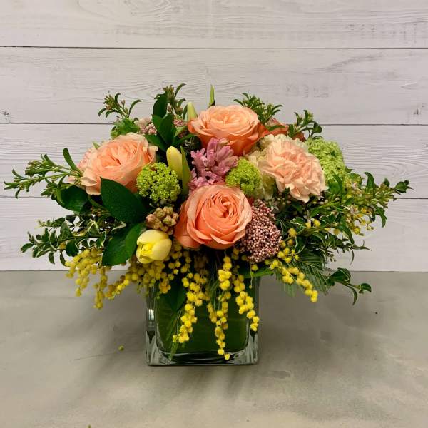 Peach roses and mixed blooms arranged in a square glass vase