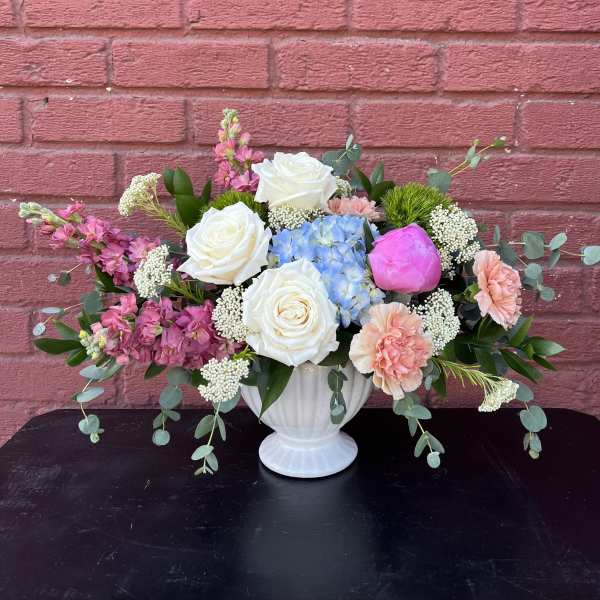 Mixed bouquet in a white vase with white roses, blue hydrangea, and pink blooms