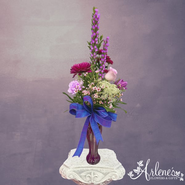 Purple and pink floral arrangement in a tall vase with a blue ribbon