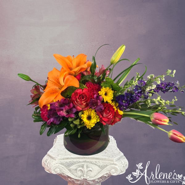 Colorful bouquet with orange lilies, red roses, yellow daisies, and purple flowers in a dark vase