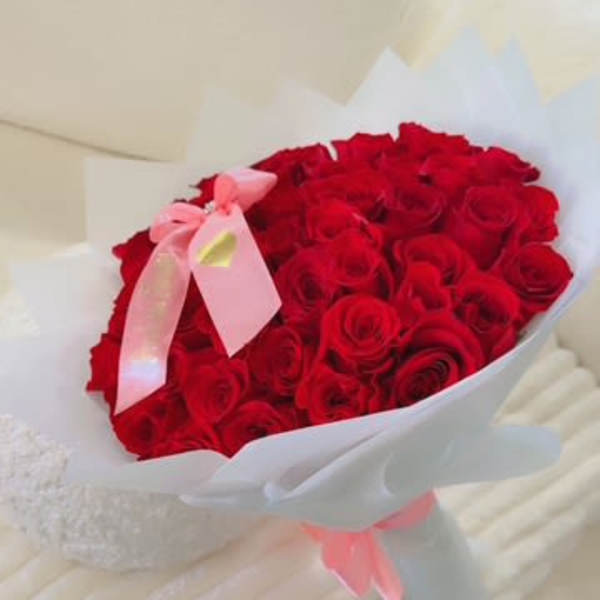 Bouquet of red roses wrapped in white paper with a pink ribbon