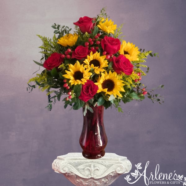 Bouquet of red roses and yellow sunflowers in a burgundy glass vase