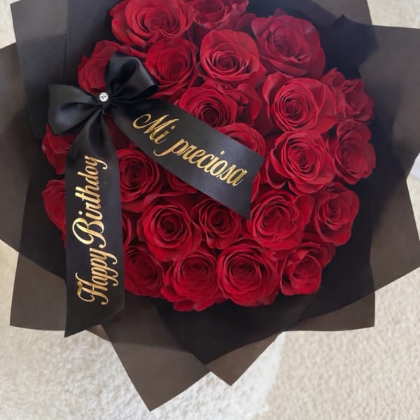 Round bouquet of red roses wrapped in black paper with a black birthday ribbon bow