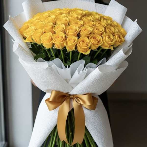 Bouquet of yellow roses wrapped in white paper with a gold ribbon