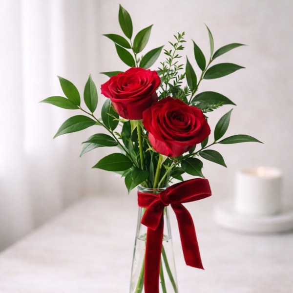 Two red roses in a clear glass vase with a red ribbon