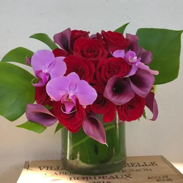 Red roses and purple orchids arranged in a glass vase