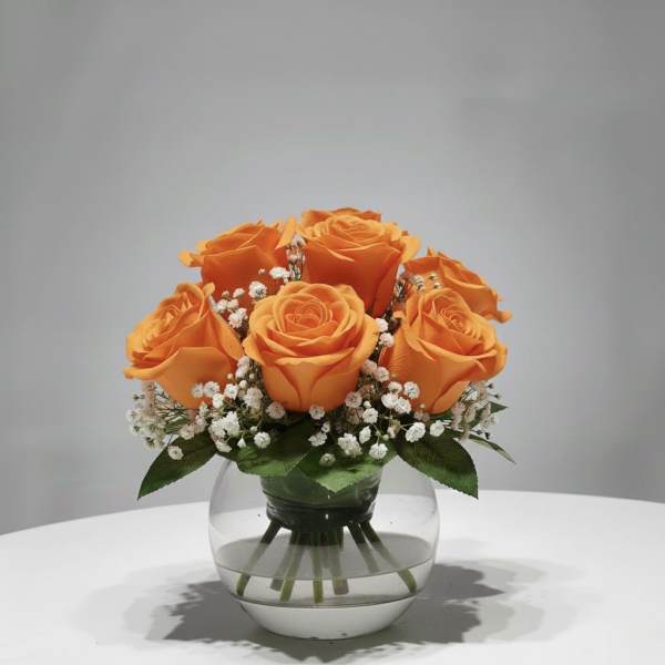 Orange roses arranged in a clear glass vase with white filler flowers