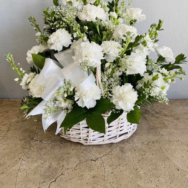 White floral arrangement in a wicker basket with a satin ribbon