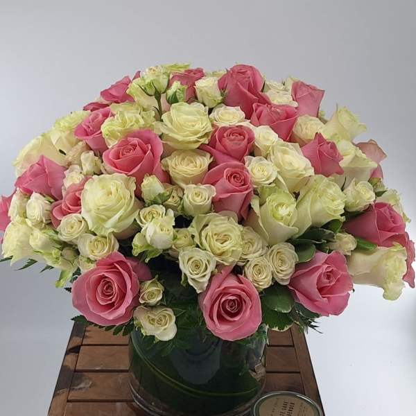 Pink and white roses arranged in a glass vase with a candle beside it